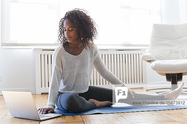 Frau benutzt Laptop auf Yogamatte