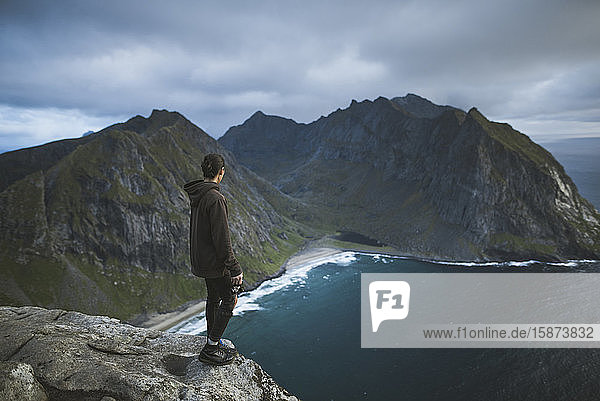 Mann hält Kamera auf Klippe am Berg Ryten auf den Lofoten  Norwegen