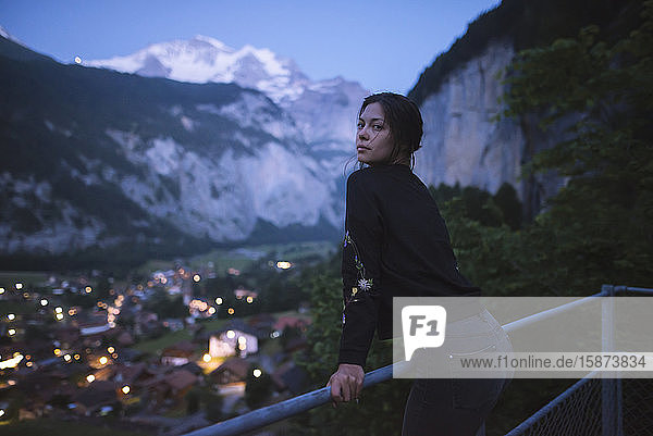 Young woman leaning on railing by mountain and village