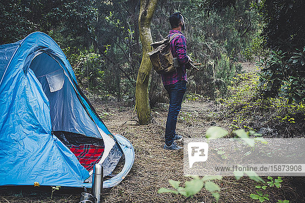 Mann hält Stöcke am Zelt im Wald