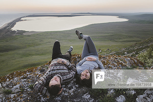 Junges Paar liegt bei Sonnenuntergang auf einem Hügel