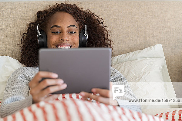 Smiling woman using tablet with headphones in bed