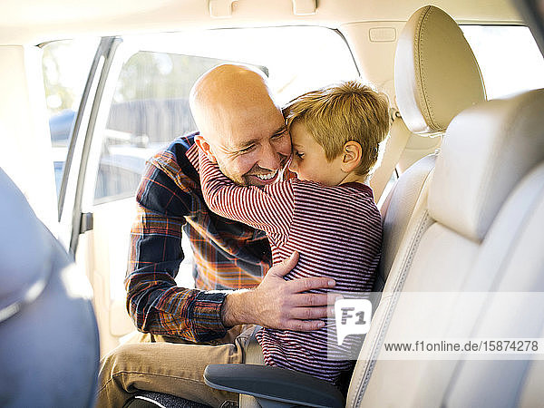 Junge sitzt im Auto und umarmt seinen Vater