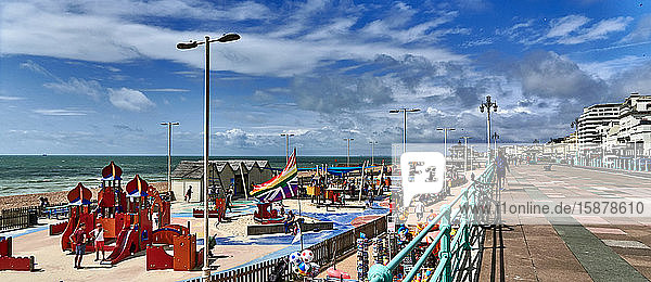 Großbritannien  East Sussex  Südküste Englands  Stadt Brighton und Hove  Foto von der Strandpromenade und dem Strand von Brighton an einem sonnigen Tag  mit Touristen  die an der Strandpromenade und auf dem Spielplatz spazieren gehen  Brighton liegt an der Südküste Englands und gehört zur Stadt Brighton und Hove. Die Lage von Brighton hat die Stadt zu einem beliebten Reiseziel für Touristen gemacht und ist das beliebteste Badeziel im Vereinigten Königreich für Touristen aus Übersee  das auch als die angesagteste Stadt des Vereinigten Königreichs bezeichnet wird.