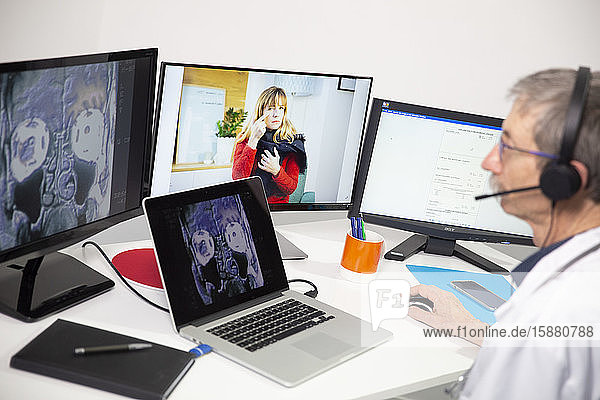 Ein Allgemeinmediziner betrachtet in einer Videosprechstunde das RÃ¶ntgenbild einer Frau  die Schmerzen in den NebenhÃ¶hlen hat.