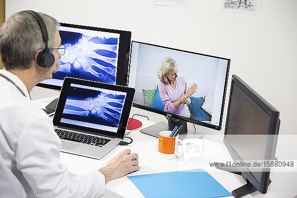Ein Rheumatologe betrachtet wÃ?hrend einer Videokonsultation die RÃ¶ntgenaufnahme der Hand eines Patienten  der an Handschmerzen leidet.