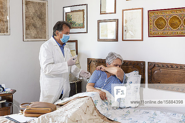 A doctor making a home visit to a senior woman patient. Woman coughing covering her mouth with her arm.