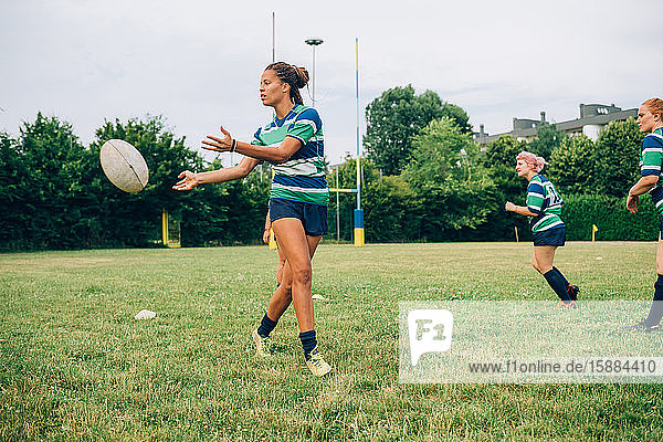 Drei Frauen in blauen  weißen und grünen Rugbyhemden auf einem Trainingsplatz  eine Frau gibt einen Rugbyball ab.