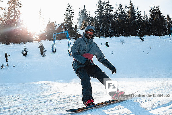 A snowboarder skiing down a snowy slope with trees and a ski lift in the background.