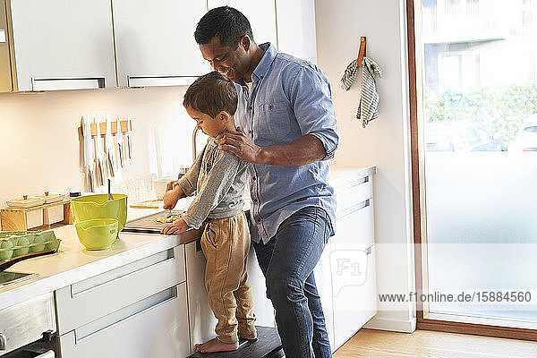 A father and son both standing at a kitchen worktop preparing food on a chopping board.