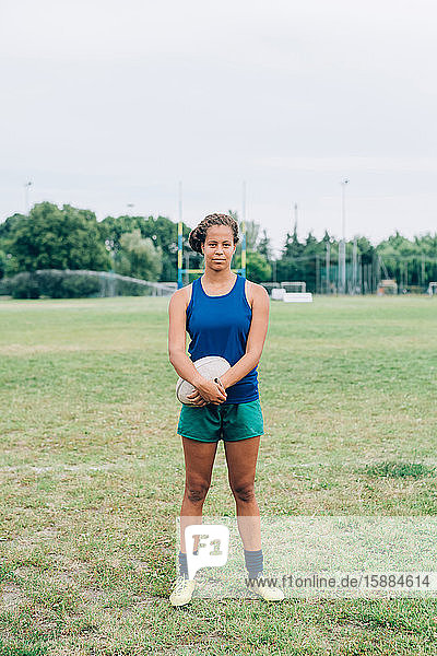 Eine Frau  die in Shorts und T-Shirt auf einem Trainingsplatz steht und einen Rugbyball hält.