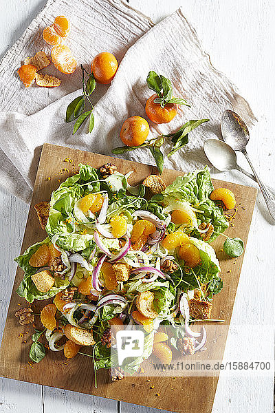 Draufsicht auf ein Holzbrett mit einem Salat mit roten Zwiebeln  Croutons  Orangensegmenten und Nüssen.