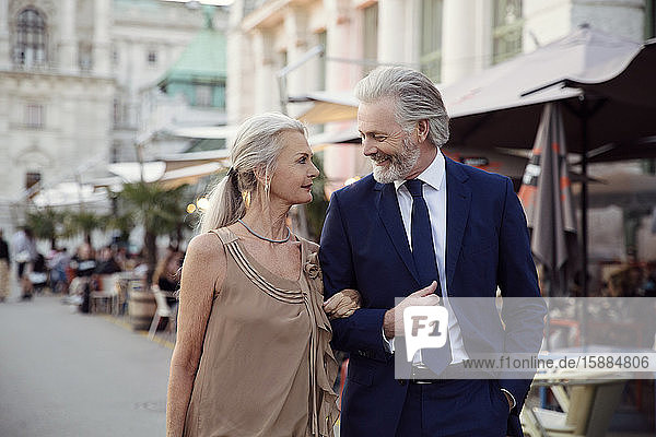 Ein Ehepaar geht Arm in Arm eine Straße mit Bars und Marktständen in Wien entlang.