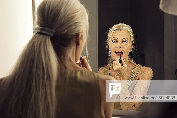 Rear view of a woman looking into a mirror and applying lipstick.