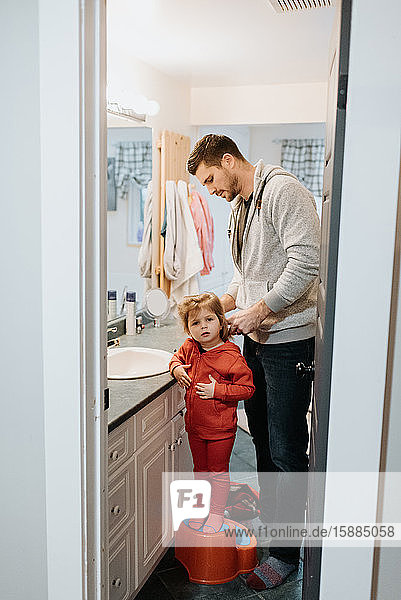 Ein Mann steht im Badezimmer und bürstet seinem Kind die Haare.