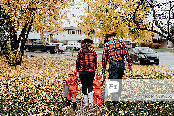 Eine Familie mit zwei Kindern  die für Halloween als Feuerwehrmänner verkleidet sind  spaziert durch einen mit Blättern übersäten Park.