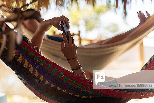 Woman checking a smart phone lying in a hammock in the shade.