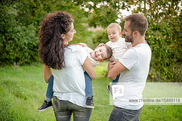 Porträt einer Familie mit zwei Kindern  die auf einer Wiese stehen  lächeln und sich umarmen.