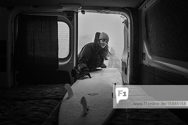 Woman putting a surfboard into the back of a campervan. Winter Surfing