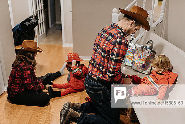 Eine Mutter und ein Vater ziehen ihren Kindern Schuhe an  die zu Halloween als Feuerwehrmänner verkleidet sind.
