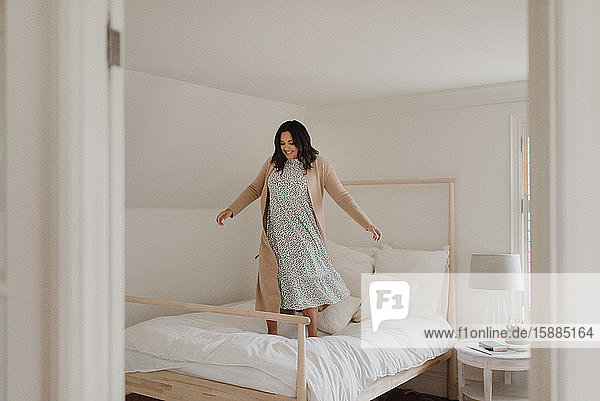 Frau mit langen dunklen Haaren springt vor Freude auf einem Bett herum.