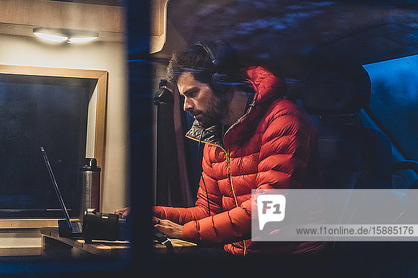 A man sitting at a table in his campervan working on his laptop.