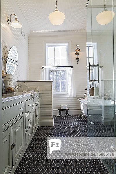 Bathroom with black tiled floor cream paneled walls and sash windows. Stand alone white bath and glass shower cubicle.