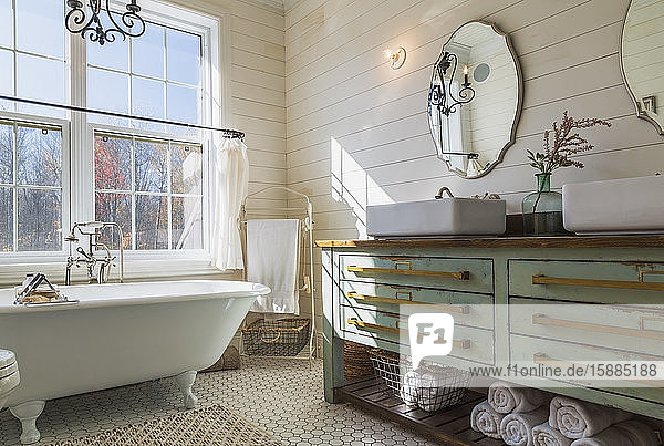 Bathroom with white roll top bath cream tiled floor and wood panelled walls green vanity unit with double hand basin.