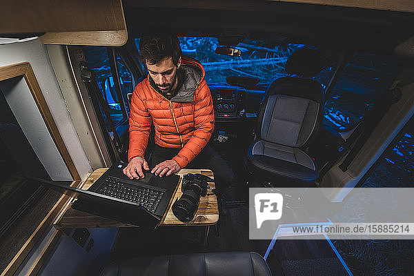 A man sitting at a wooden table in his campervan working on his laptop.