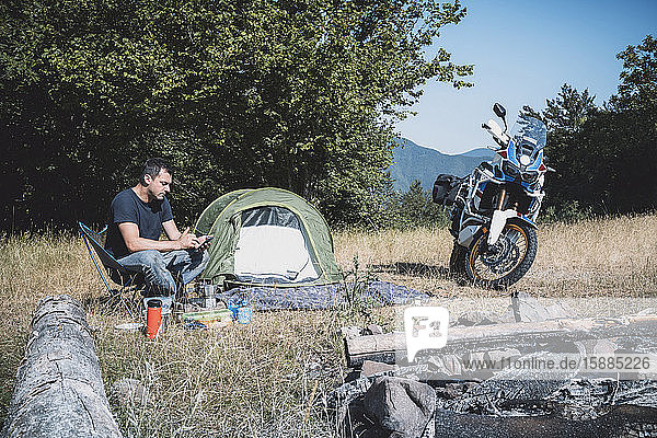 Mann auf Motorradreise beim Camping auf einer abgelegenen Wiese