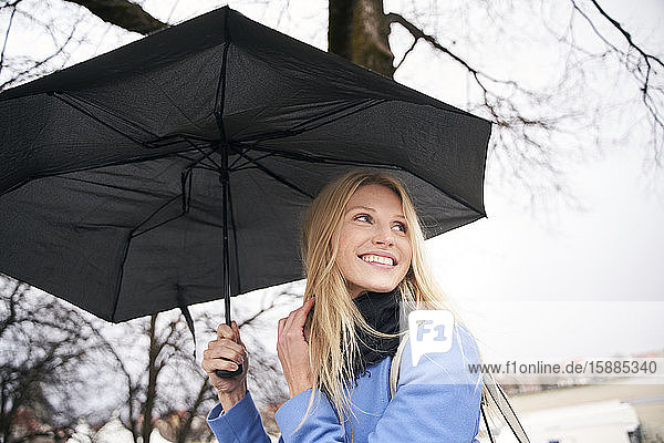Smiling blond woman holding umbrella outdoors
