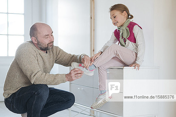 Father helping daughter putting on shoes at home