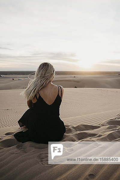 Rückenansicht einer blonden Frau  die auf einer Sanddüne sitzt und den Sonnenuntergang beobachtet  Algodones Dunes  Brawley  USA