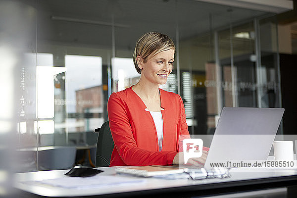 Lächelnde Geschäftsfrau benutzt Laptop im Büro