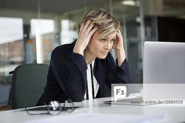 Geschäftsfrau im Büro mit dem Kopf in der Hand am Laptop