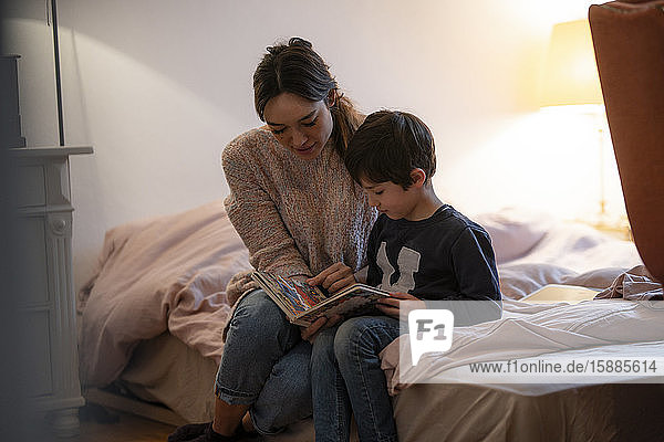 Mother and little son sitting together on bed watching picture book
