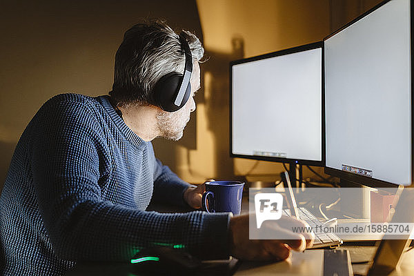 Reifer Mann sitzt zu Hause am Schreibtisch und arbeitet mit Grafiktablett und Computer