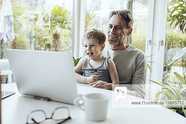 Little boy sitting on lap of father  traying to work from home