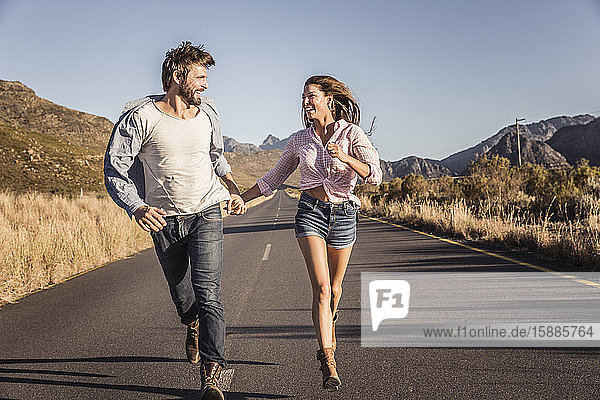 Glückliches Paar rennt auf einer Landstraße