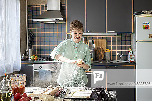 Porträt eines lachenden Jungen  der in der Küche Pizzateig zubereitet