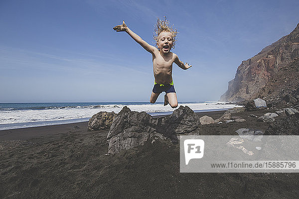 Little boy jumping for joy on a rocky beach
