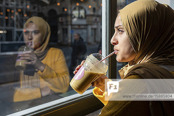 Porträt einer nachdenklichen jungen Frau  die in einem Cafe Smoothie trinkt
