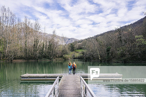 Back view of two women with backpacks standing on jetty  Valdemurio Reservoir  Asturias  Spain