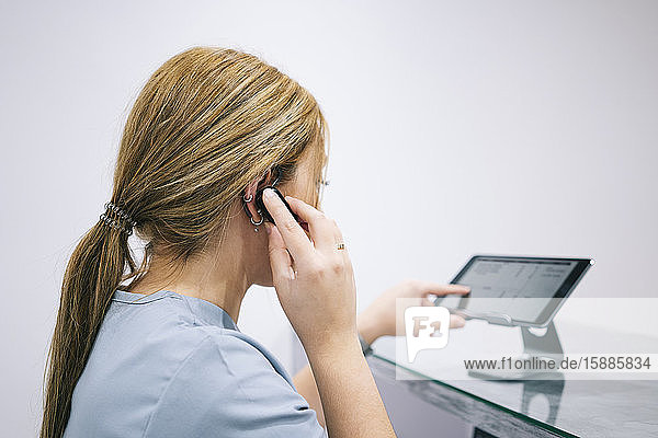 Empfangsdame an der Rezeption einer Arztpraxis mit Kopfhörer und Digitalgerät