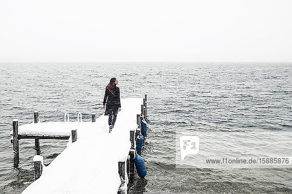 Rückenansicht einer jungen Frau  die auf einem schneebedeckten Steg am Starnberger See geht  Deutschland