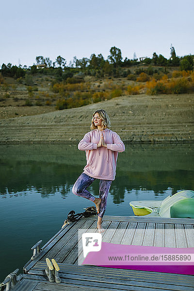 Young woman doing yoga on a jetty  tree pose