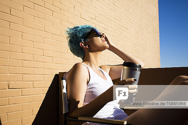 Junge Frau mit blauen Haaren gießt sich auf dem Balkon Wasser über den Kopf