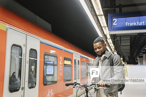 Stylish man with a bicycle  headphones and smartphone in a metro station