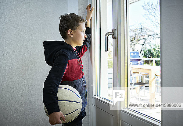 Trauriger Junge mit Basketball  der aus dem Fenster schaut