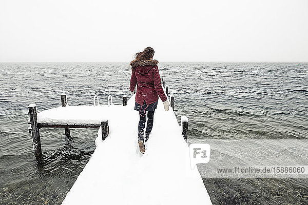Rückenansicht einer jungen Frau  die auf einem schneebedeckten Steg am Starnberger See läuft  Deutschland